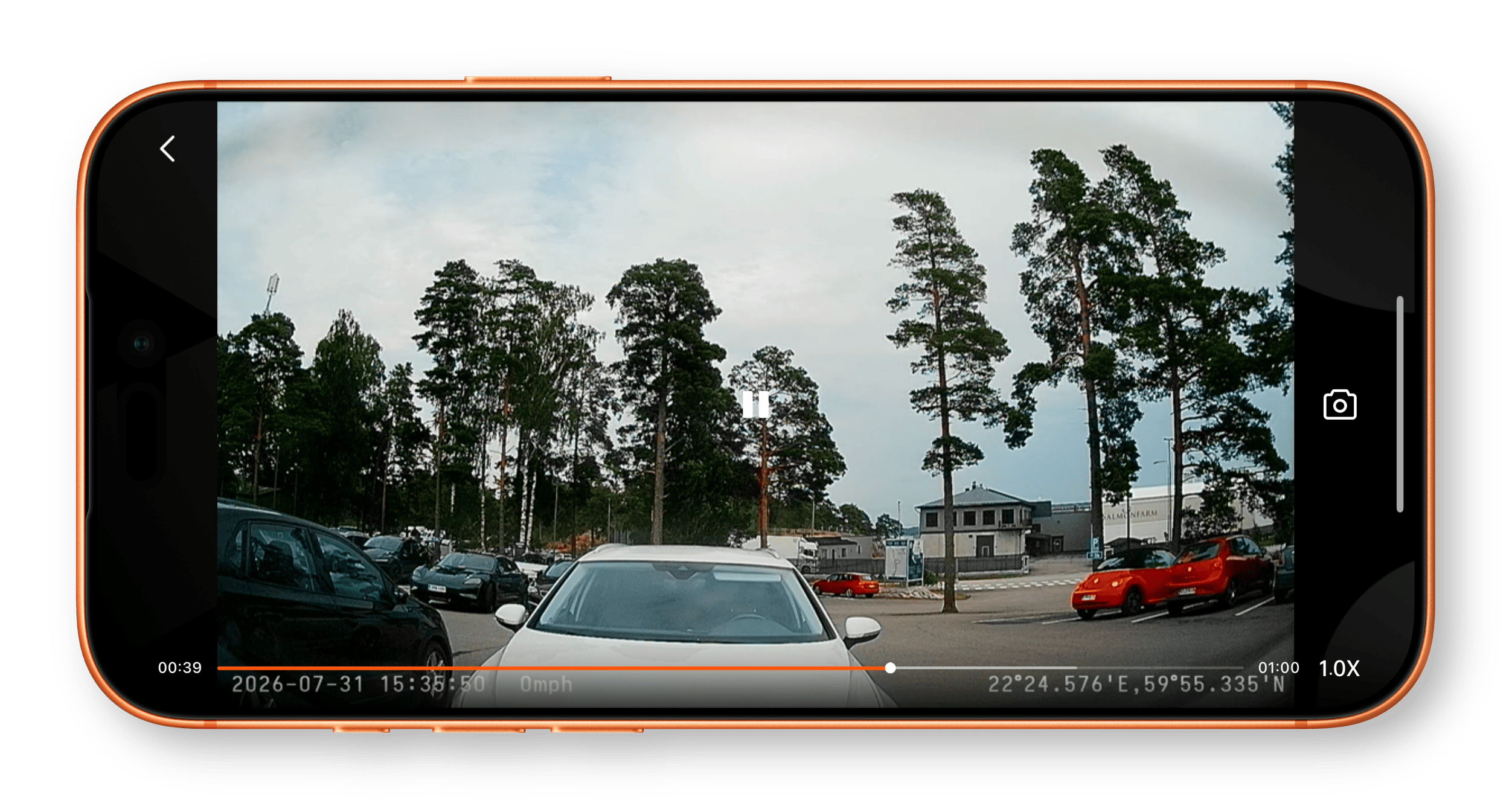 Ein Smartphone-Display zeigt eine Dashcam-Aufnahme eines Parkplatzes mit Autos, Bäumen und einem Gebäude, ergänzt durch Einblendungen von Zeitstempel, Geschwindigkeit und GPS-Daten.