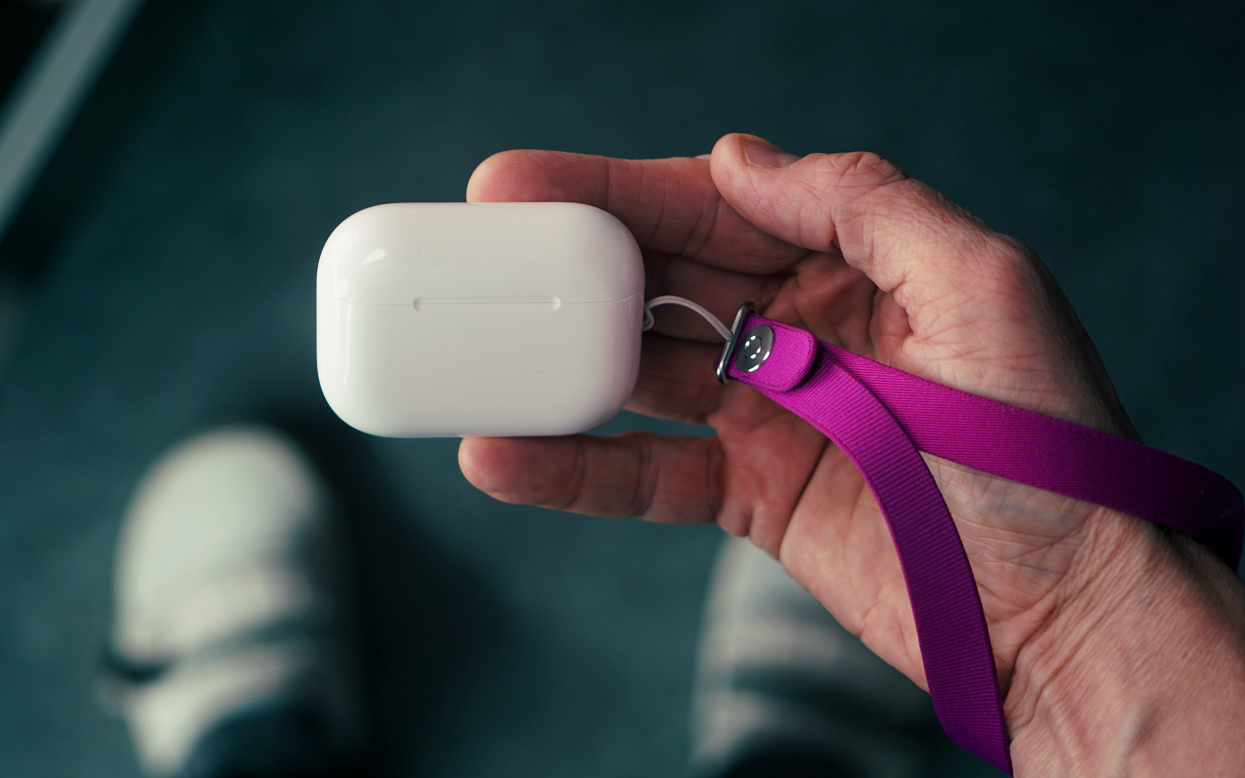 A person's hand holding a white earbud charging case attached to a purple lanyard.